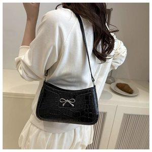 Detail of black crocodile embossed shoulder bag with a silver metal bow accent