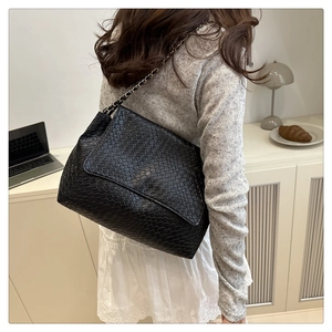 Detail of black woven shoulder bag with chic silver chain strap on a model's back
