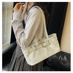 Detail of a creamy white glossy patent leather handbag with metallic buckle strap
