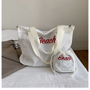 Close-up of white canvas tote bag with red Beach text and matching drawstring pouch