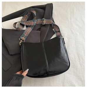 Detail of glossy black leather moon bag with wide bohemian geometric strap