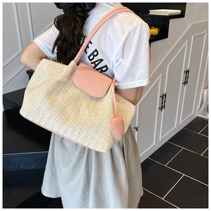 Detail view of woven straw tote bag featuring pink leather flap and heart-shaped charm