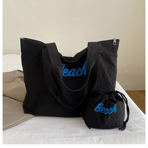 Detail of black canvas tote bag and drawstring pouch set with blue Beach lettering