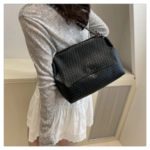 Detail of black woven texture on flap crossbody bag with metal chain strap