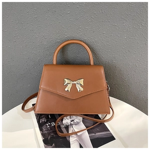 Detail of a brown trapezoid handbag with a golden bow buckle on a magazine background
