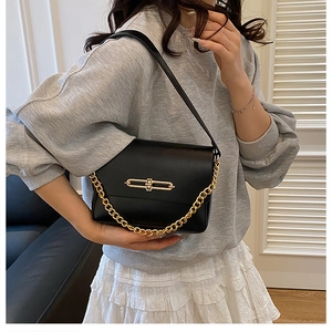 Detail of black matte crossbody bag with distinctive gold metal buckle and chunky chain