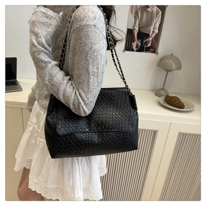 Détail d'un sac bandoulière en cuir tressé noir avec bandoulière chaîne sur modèle
