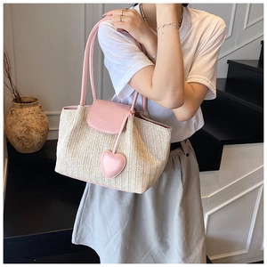 Detail of woven straw tote bag with pink leather straps and heart charm on stairs