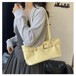 Detailed shot of pale yellow shoulder bag with glossy leather and metallic buckle strap