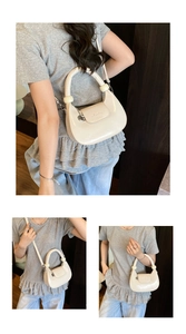 Detail of a creamy white crescent bag featuring a thick top handle and silver heart charm