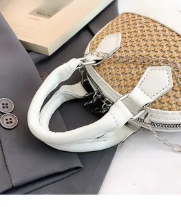 Detail of woven straw shell bag with white leather handle and silver metal chain strap