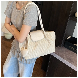 Detail of cream straw tote bag featuring white leather trim and heart pendant detail