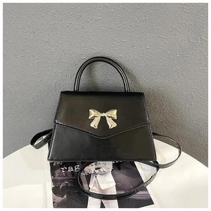Detail of a black trapezoid handbag featuring a polished gold bow buckle on the flap