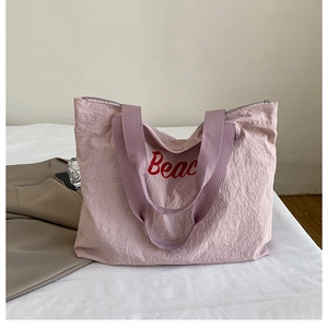Detailed macro view of pink crinkle fabric tote bag featuring red Beach lettering