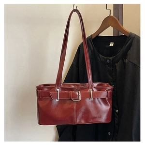 Close-up of wine red glossy leather handbag featuring decorative silver buckle and thin straps