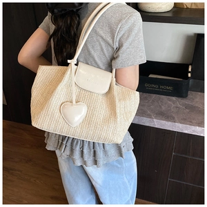Detailed close-up of straw woven tote bag featuring white leather flap and heart charm