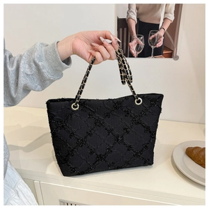 Detail of black quilted tote bag featuring shimmering fabric and gold chain strap