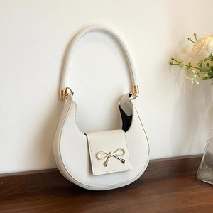 Detail view of cream crescent bag featuring saffiano leather and gold bow hardware