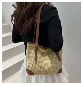 Close-up of woven straw tote bag with brown faux leather corners and adjustable shoulder strap
