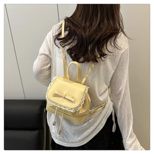 Détail d'un mini sac à dos jaune clair avec bordure en dentelle blanche et petit nœud