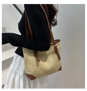 Close-up of woven straw tote bag with brown leather straps shown on model shoulder