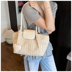 Detail of hand-woven straw tote bag featuring beige leather flap and heart pendant