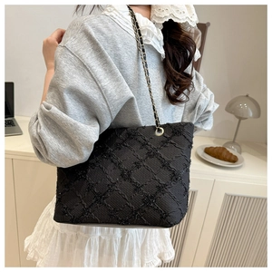 Detail view of large black quilted tote bag with gold-intertwined chain shoulder strap