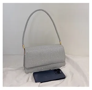 Pochette enveloppe pailletée argentée avec chaîne, montrée à côté d'un smartphone
