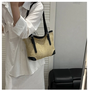 Model wearing a woven straw tote bag with black leather straps and metal buckles