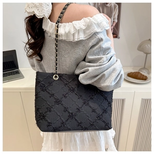 Detail of black quilted tote bag with sequins and gold chain strap on shoulder