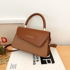 Brown woven crossbody bag with leather flap and gold fashion logo on wooden surface