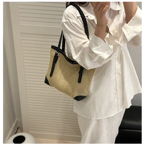 Detail of woven straw tote bag with black leather straps and metal buckle on a model
