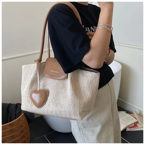 Detail of woven straw tote bag with brown faux leather flap and heart-shaped charm
