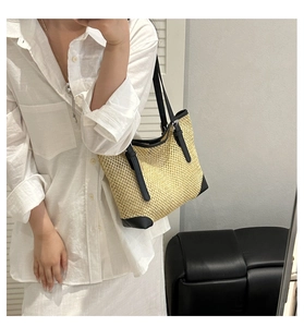 Detail of woven straw tote bag featuring black faux leather trim and thin double handles