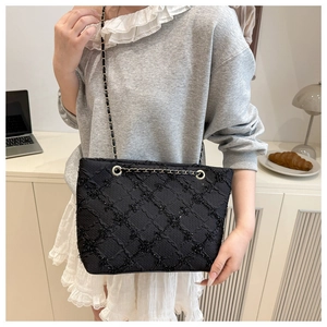 Detail of black quilted tote bag with gold chain strap carried by a model in a minimal room