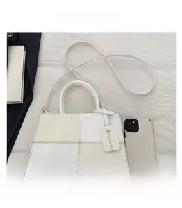 Detailed comparison of colorblock handbag size with a smartphone for scale reference