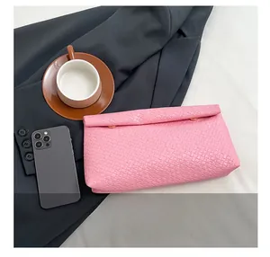 Pink woven leather clutch bag shown with a coffee cup and phone to display actual size