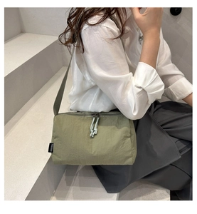 Detail of olive green nylon tote bag featuring adjustable strap and knotted zipper pulls