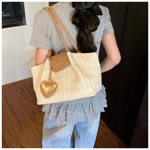 Close-up of beige straw tote bag with brown leather flap and heart-shaped charm detail
