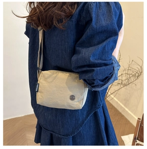 Detail of beige crossbody bag with adjustable strap and logo tag worn by a model