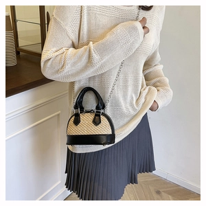 Detailed view of woven straw shell bag with black leather trim and silver chain strap