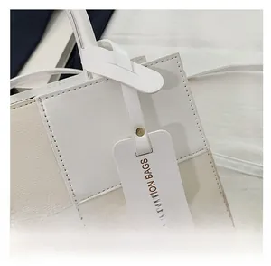 Detail of the stitched checkered design and decorative tag on this white fashion tote bag