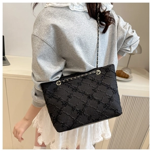 Detail of black quilted tote bag with chain strap shown in a minimalist office setting