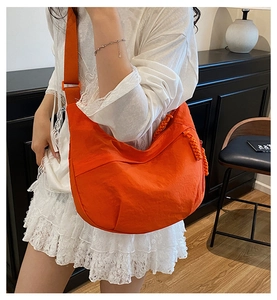 Détail du sac besace en nylon orange vif avec bandoulière large et tirette de zip tissée