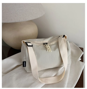 Detail of off-white cylindrical crossbody bag showing zipper closure and adjustable strap