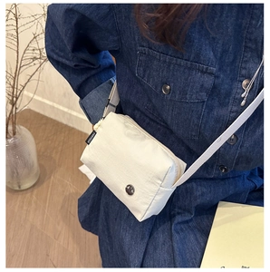 Detail of minimalist beige nylon crossbody bag featuring a round logo and Fanyissa woven tag