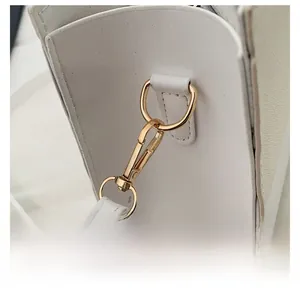 Detailed close-up of golden detachable metal hook hardware on white leather handbag
