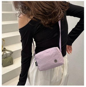 Close-up of a purple nylon crossbody bag side profile featuring a black woven brand label