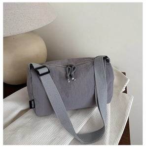 Detail of grey nylon cylinder crossbody bag with double zippers and woven shoulder strap