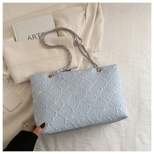 Detailed shot of light blue textured tote bag with white bow embroidery and chain strap